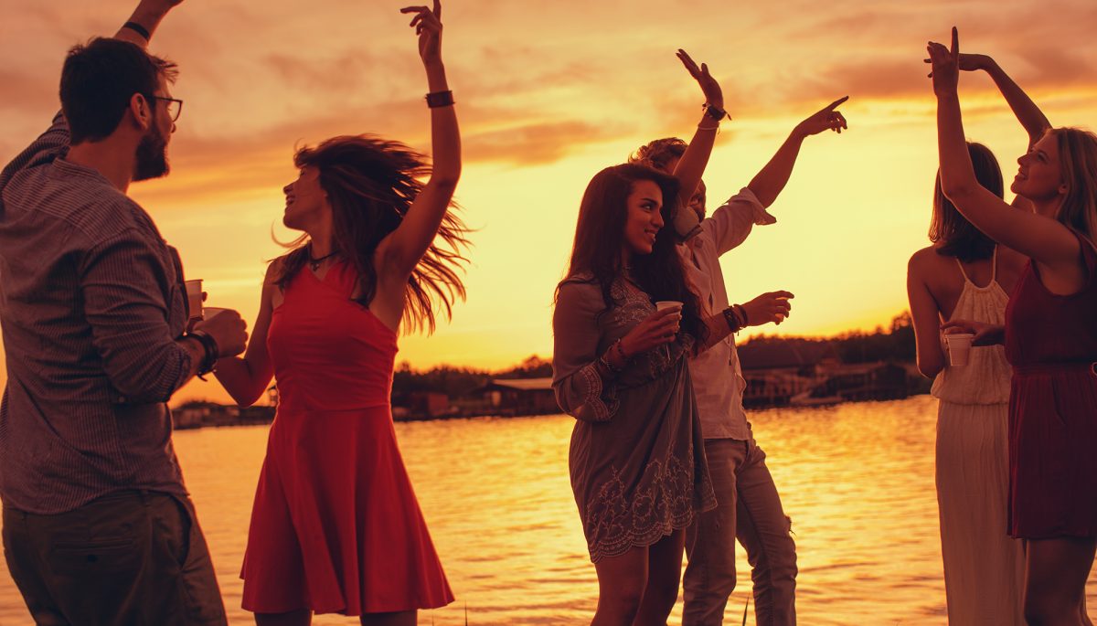 Group of young people have a party by the river during the sunset